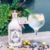 A Boothstown Gooseberry Gin and tonic in a glass next to a bottle of Boothstown Gooseberry gin